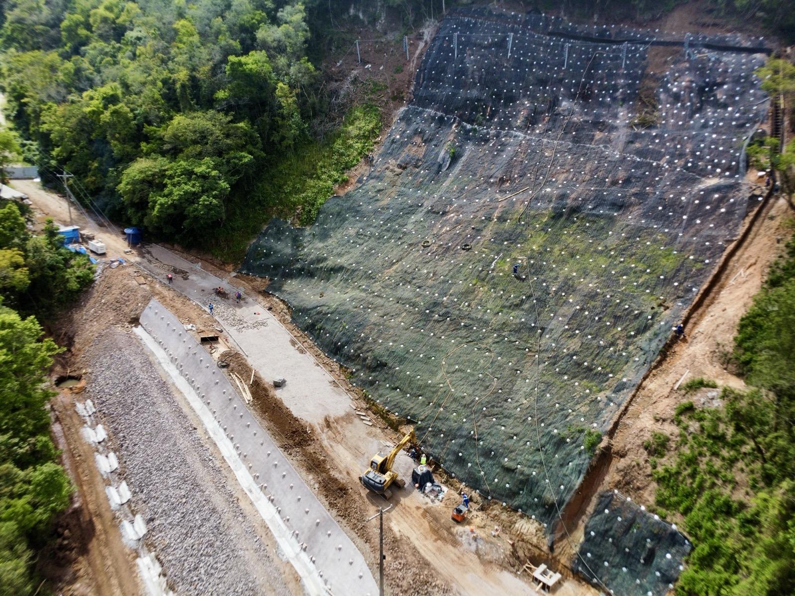 Vista aérea da obra de contenção na Estrada do Perau, em Santa Maria, com a encosta coberta por manta e máquinas trabalhando no trecho, em 21 de outubro de 2026